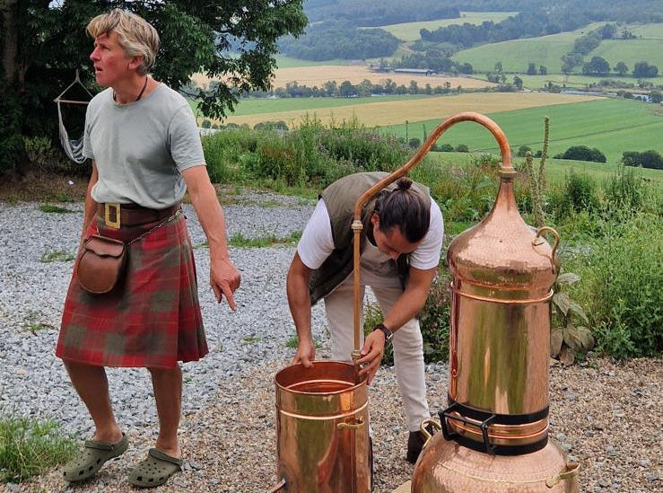 Hamish and Victor Alarcón wearing traditional Scottish kilts working with a copper outdoors